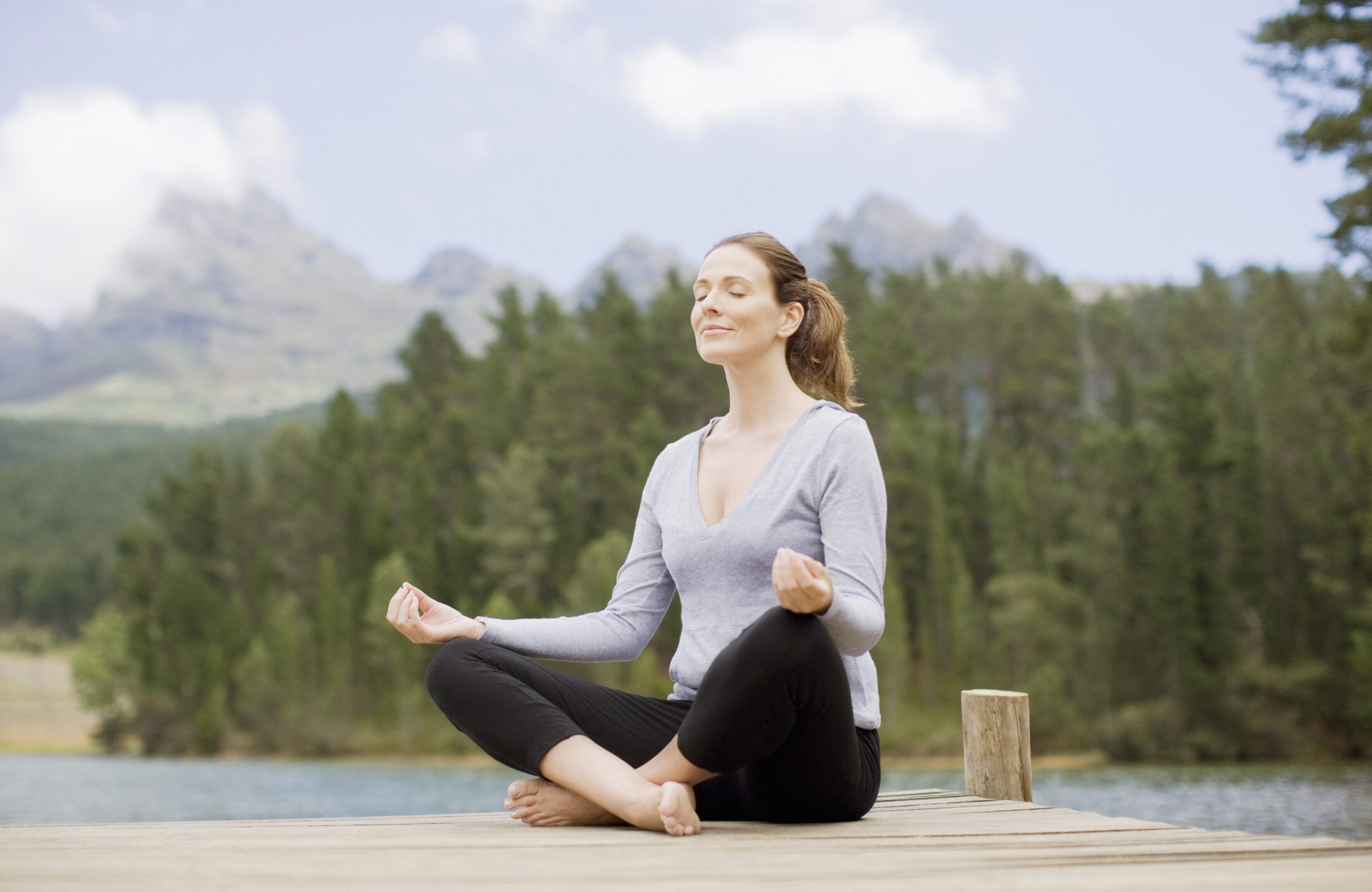 Woman practicing yoga on pier by lake